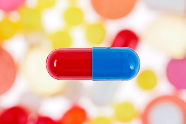 One capsule (pill) macro view on blurred multicolored drugs back — Stock Photo, Image