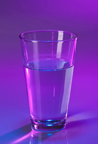 Glas met water op violette achtergrond — Stockfoto