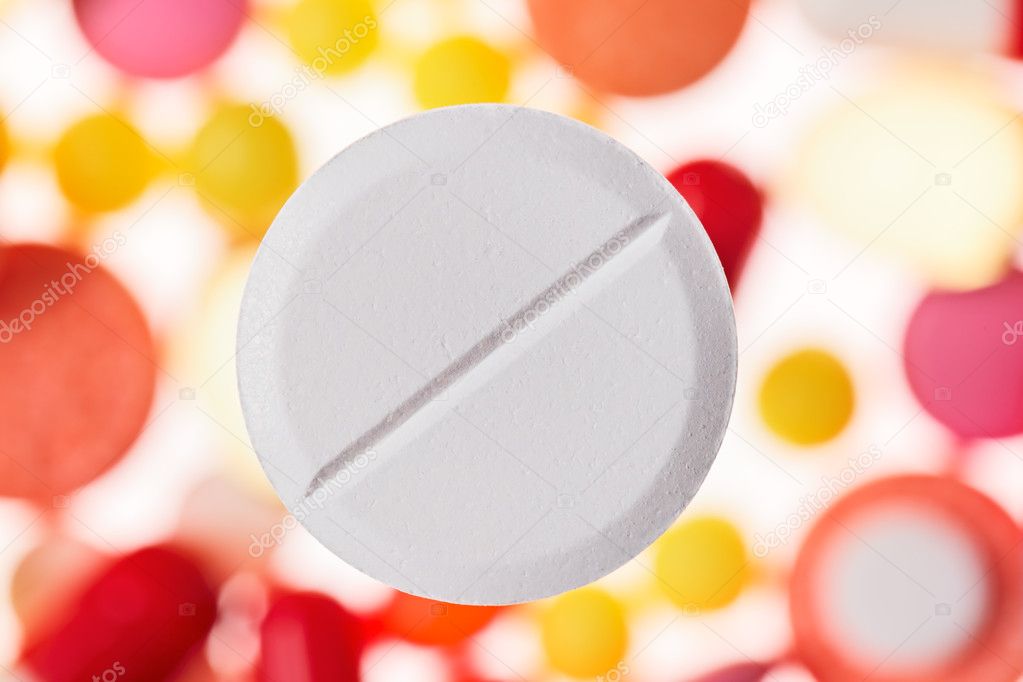 One big tablet (pill) macro view on blurred multicolored drugs b