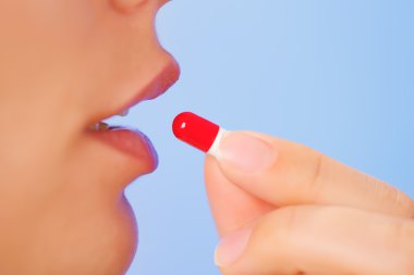 Young woman taking red and white bolus (capsule), macro view clipart