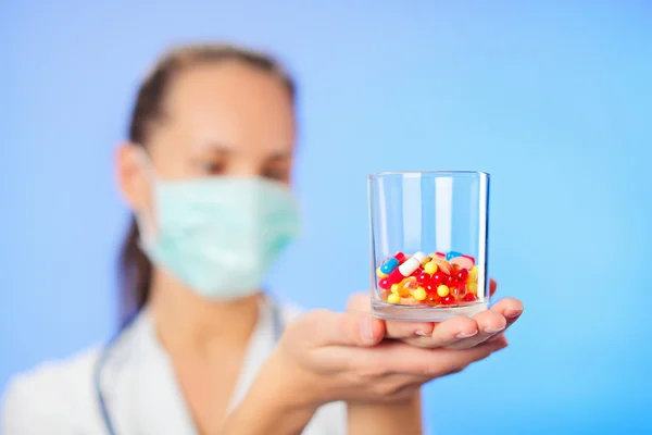 Pastillas, tabletas y medicamentos amontonan en la mano del médico sobre fondo azul — Foto de Stock