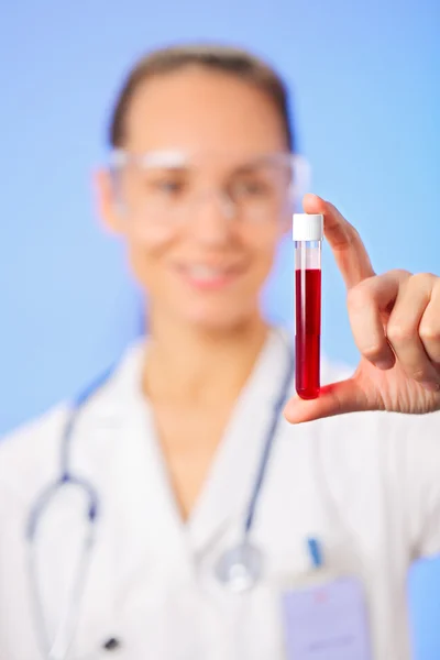 Tubo de ensayo con muestra de sangre en la mano del médico sobre fondo azul — Foto de Stock