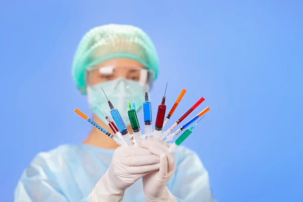 Mujer joven doctora con muchas jeringas multicolores en las manos en blu — Foto de Stock