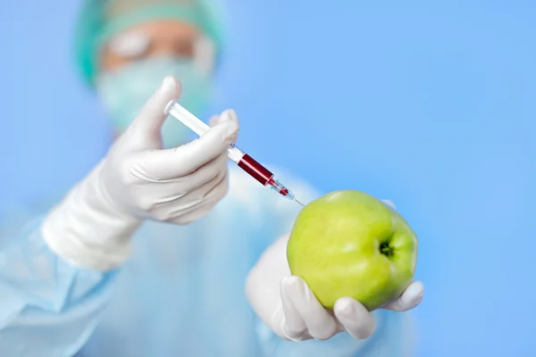 Молодая женщина доктор инъекции зеленого яблока со шприцем на синий — стоковое фото