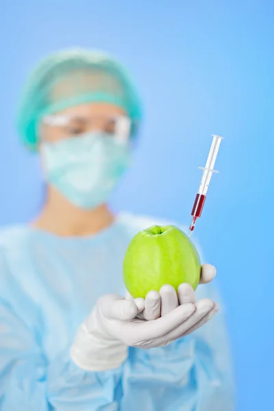 Mujer joven médico inyectando manzana verde con jeringa en azul — Foto de Stock