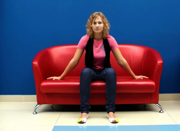 Jeune femme assise sur un canapé rouge — Photo