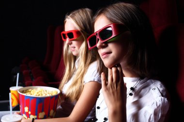 Two young girls watching in cinema clipart