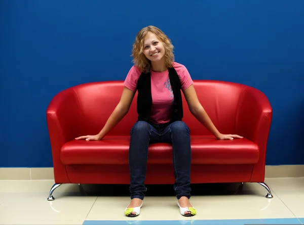 Fiatal nő ül a piros kanapé — Stock Fotó