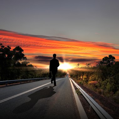 Man walking away at dawn along road clipart