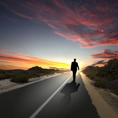 Man walking away at dawn along road clipart