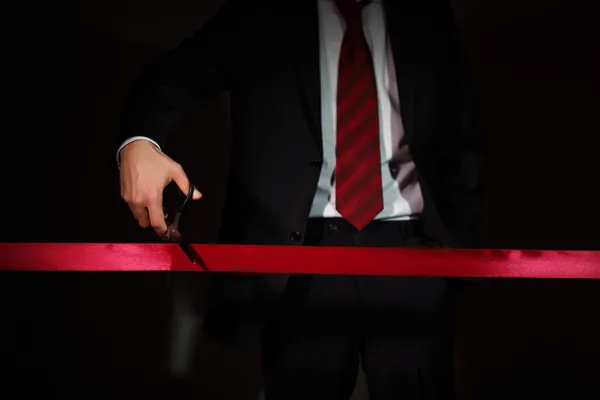 Geschäftsmann schneidet mit Schere ein rotes Band durch — Stockfoto