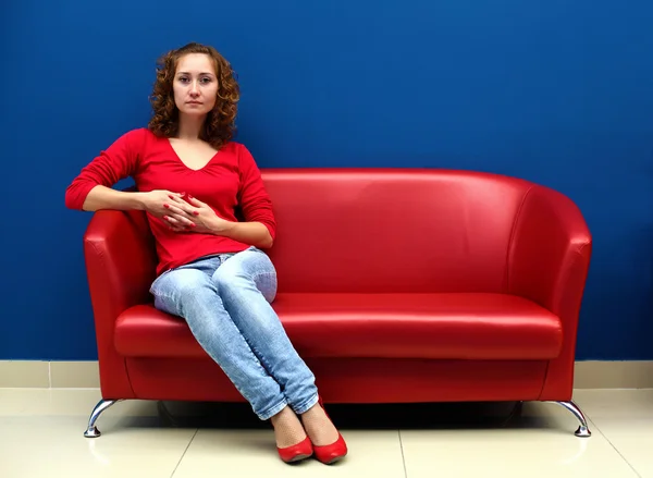 Νεαρή γυναίκα που κάθεται στον κόκκινο καναπέ — Φωτογραφία Αρχείου