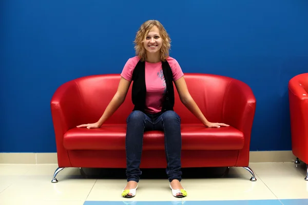 Молода жінка сидить на червоному дивані — стокове фото