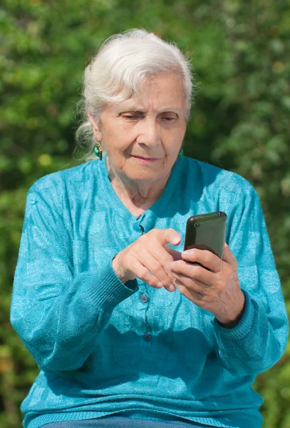 Uma mulher idosa com um telefone celular moderno nas mãos — Fotografia de Stock