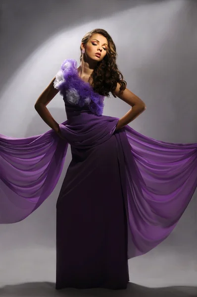 在灰色的背景上的紫色裙子美丽的女人 — 图库照片