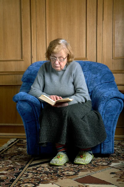 Mormor sitter i en fåtölj och läser — Stockfoto