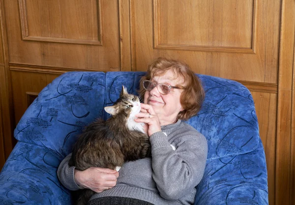 Den gamla kvinnan sitter i en fåtölj och stroke en katt — Stockfoto