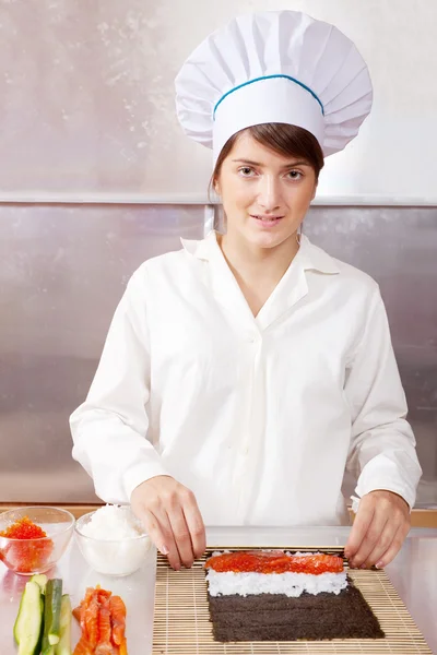 Cook woman making sushi rolls in kitchen