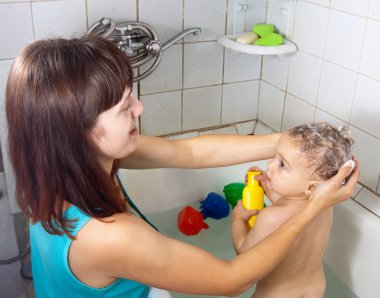 Mother wasing baby in bath clipart