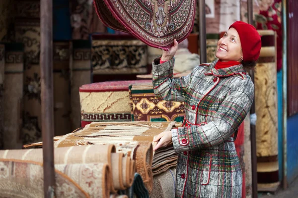 Volwassen vrouw kiest tapijt — Stockfoto