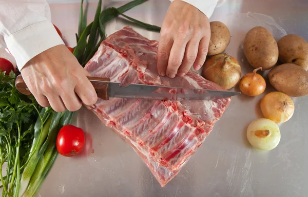 Mãos de cozinheiro cortando carne crua — Fotografia de Stock