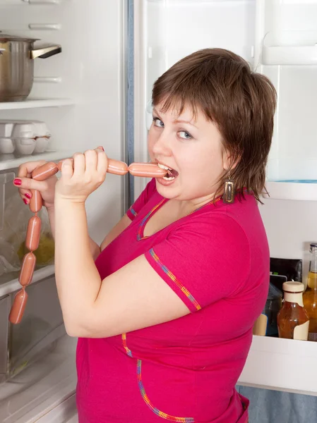 Hungry woman eating sausages from fridge — Stock Photo, Image
