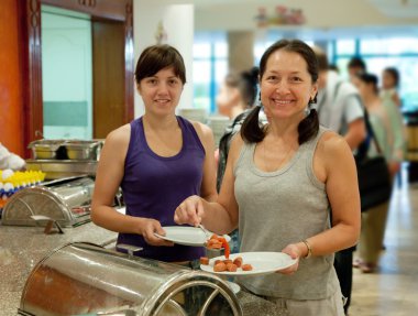 Women takes sausages in buffet clipart