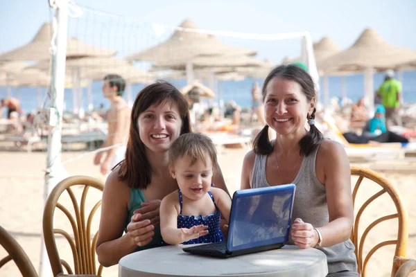 Happy women and girl with laptop at beach — Stock Photo, Image