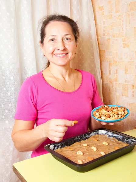 Mature woman adds nuts into dough. — Stock Photo, Image