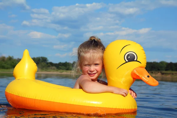 Маленькая девочка купается в реке в надувной утке — стоковое фото