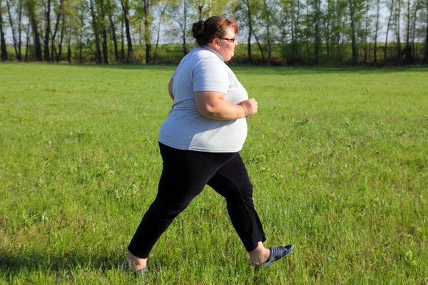 Übergewichtige Frau läuft auf Wiese Stockfoto