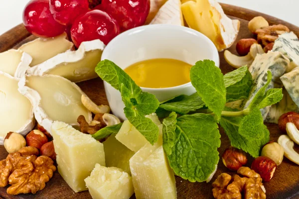 Olika sorters ost med honung, nötter och druvor på plattan, är — Stockfoto