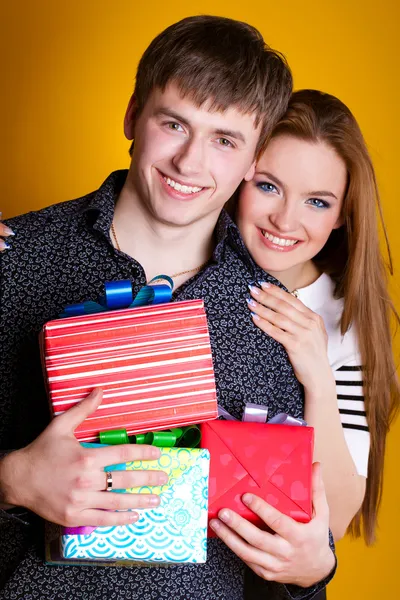 Young couple with gifts on yellow — Stock Photo, Image