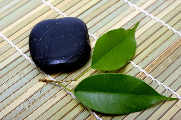 Green leaves and stones on bamboo mat — Stock Photo, Image