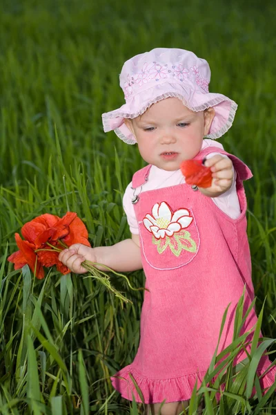Criança com flor vermelha entre grama verde — Fotografia de Stock