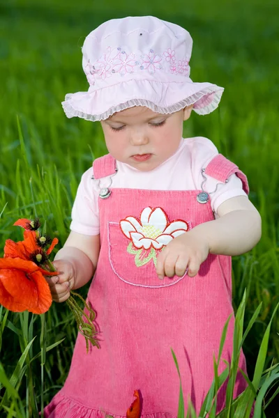 Dziecko z czerwonym kwiatem wśród zieleni trawy — Zdjęcie stockowe