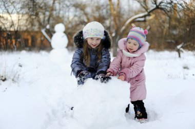 Two sisters rolling snow to make snowman clipart