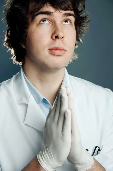 Młody lekarz w rękawice modląc się — Zdjęcie stockowe