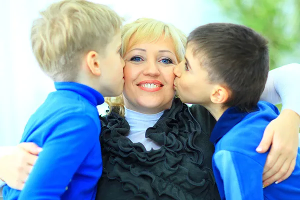 Synowie dając pocałunek matki relaksujący na kanapie — Zdjęcie stockowe