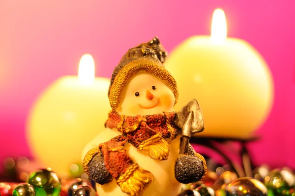 Figura muñeco de nieve y velas ardientes sobre fondo rosa romántico —  Fotos de Stock