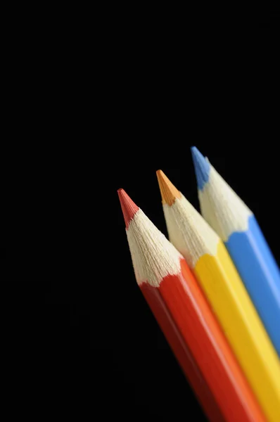 Lápis vermelhos, amarelos e azuis sobre fundo preto — Fotografia de Stock