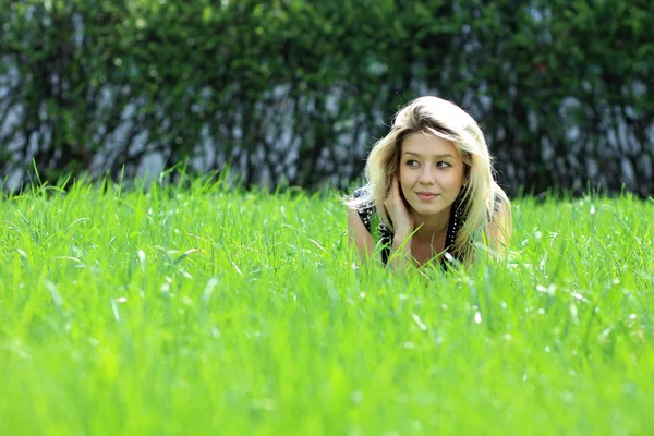 Блондинка лежить на полі трави в парку — стокове фото