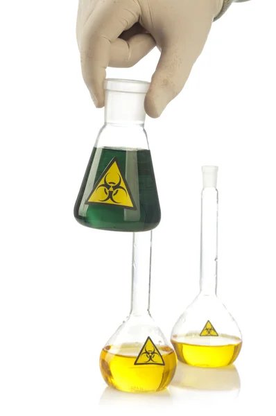 Mano sostiene el tubo de vidrio con el líquido verde y riesgo biológico símbolo. — Stockfoto
