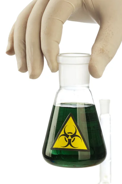 Mano sostiene el tubo de vidrio con el líquido verde y riesgo biológico símbolo. — Stockfoto