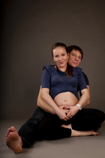 Молода доросла пара обіймається, з вагітними жінками — стокове фото