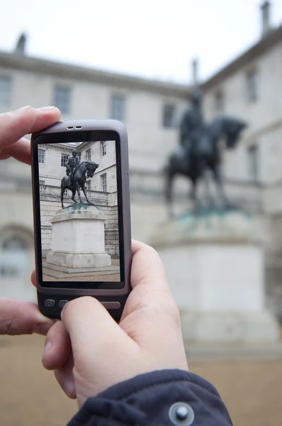 Toeristische houdt omhoog cameratelefoon bij Nelsons monument — Stockfoto