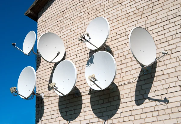 Семь спутниковых тарелок на белой стене — стоковое фото