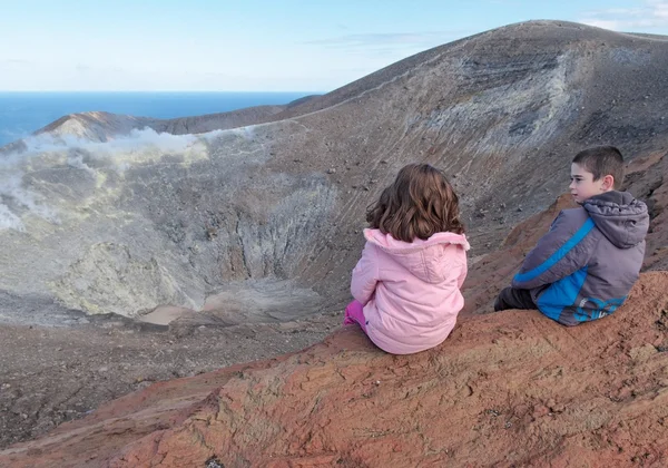Meisje en jongen zitten op de rand van de vulkaan krater — Stockfoto