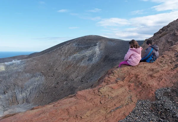 Girl and boy sitting on the rim of volcano crater — Stock Photo, Image