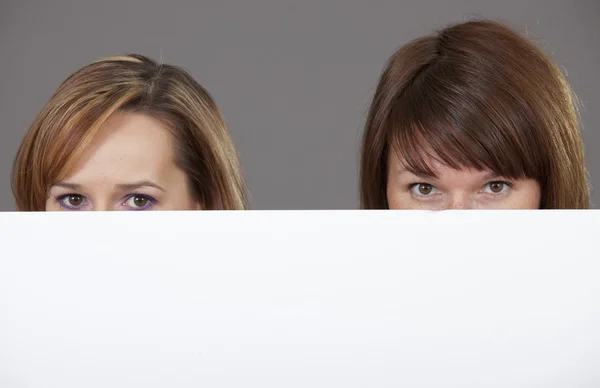 Two women peeking over white banner — Stock Photo, Image